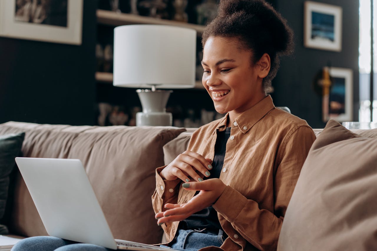 A young woman smiles while studying on a laptop in a cozy indoor setting.