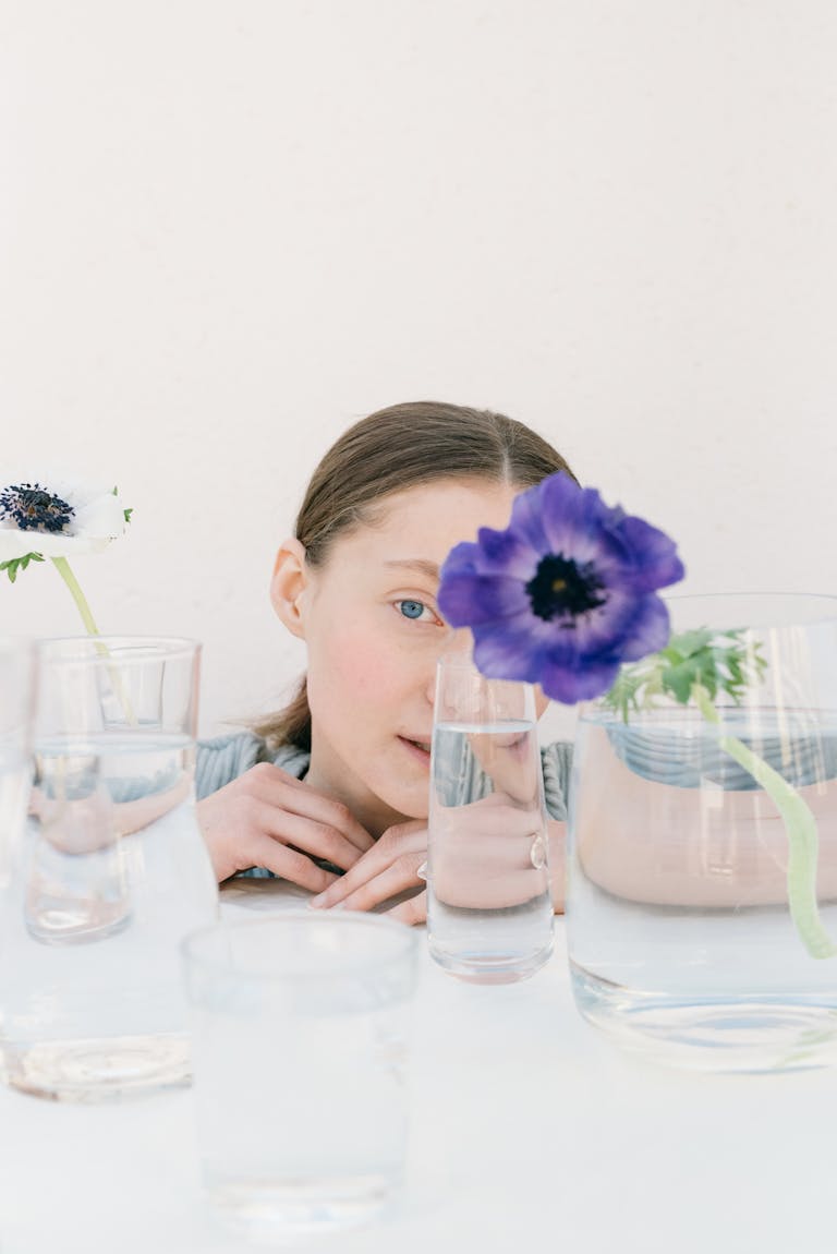 Artistic portrait of a woman behind glass and flowers, creating a distorted effect.