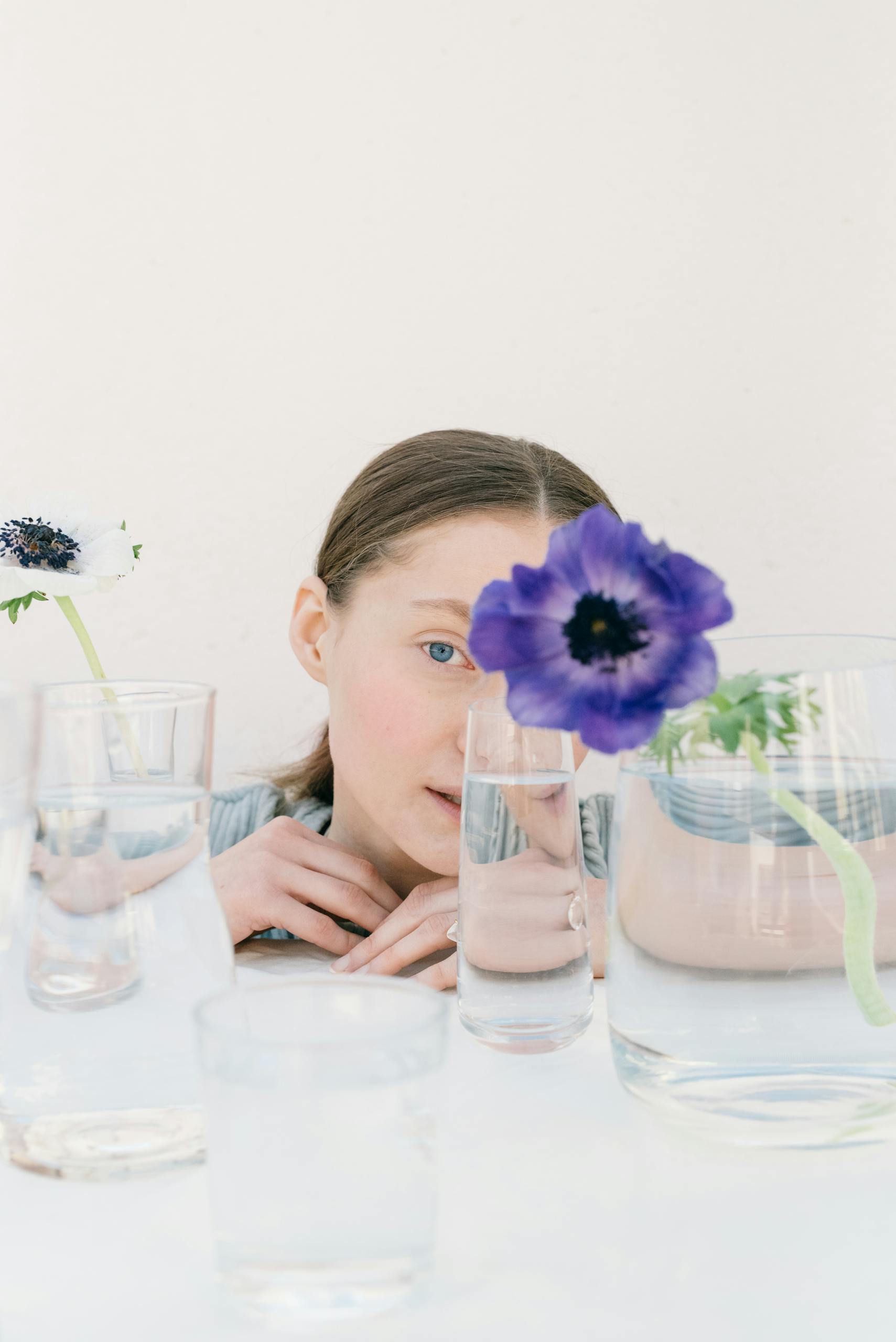 Artistic portrait of a woman behind glass and flowers, creating a distorted effect.