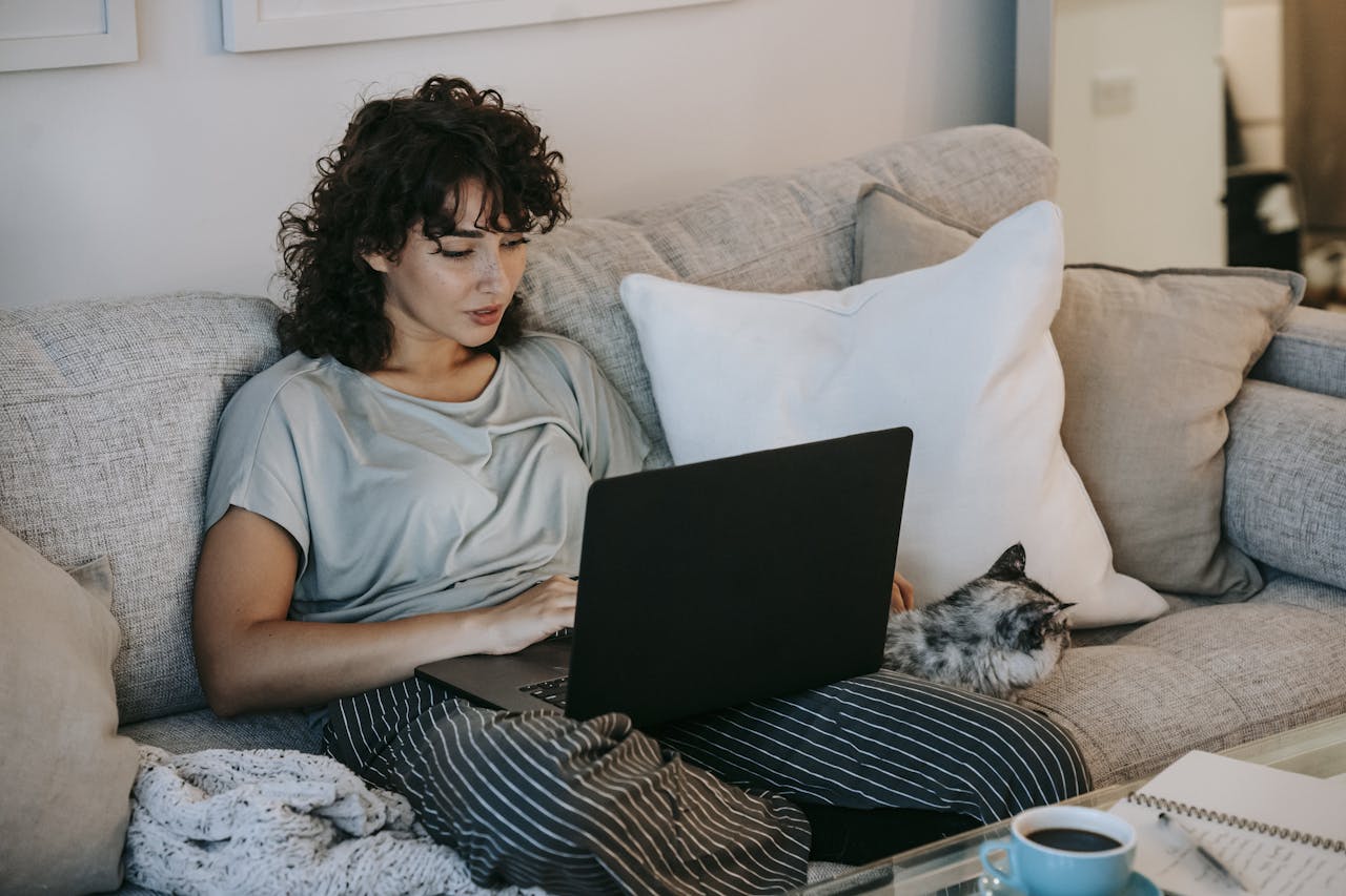 A young woman with curly hair relaxes on a cozy sofa, getting ERP Therapy on her laptop.