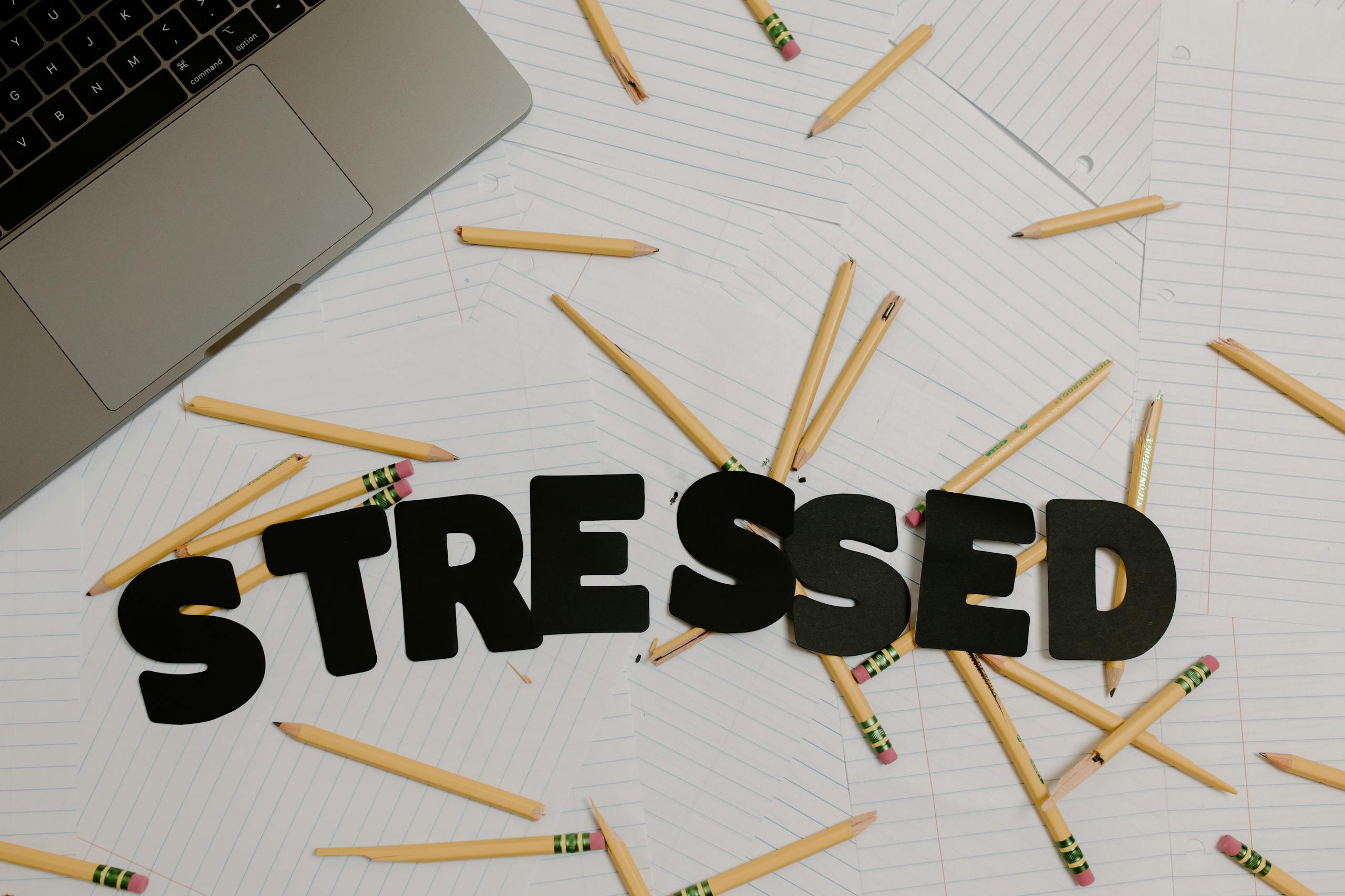 Overhead view of a stressed workplace setup with broken pencils scattered around a laptop.