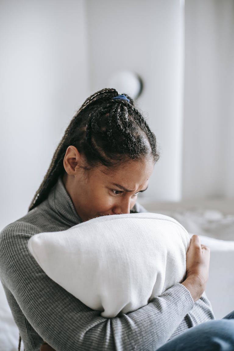 Pensive woman sitting indoors, clutching a pillow with a worried expression.