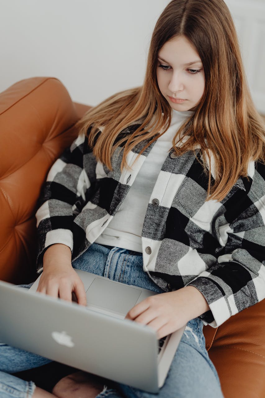 Teenage girl sitting on sofa with a laptop, engaged in online erp therapy.