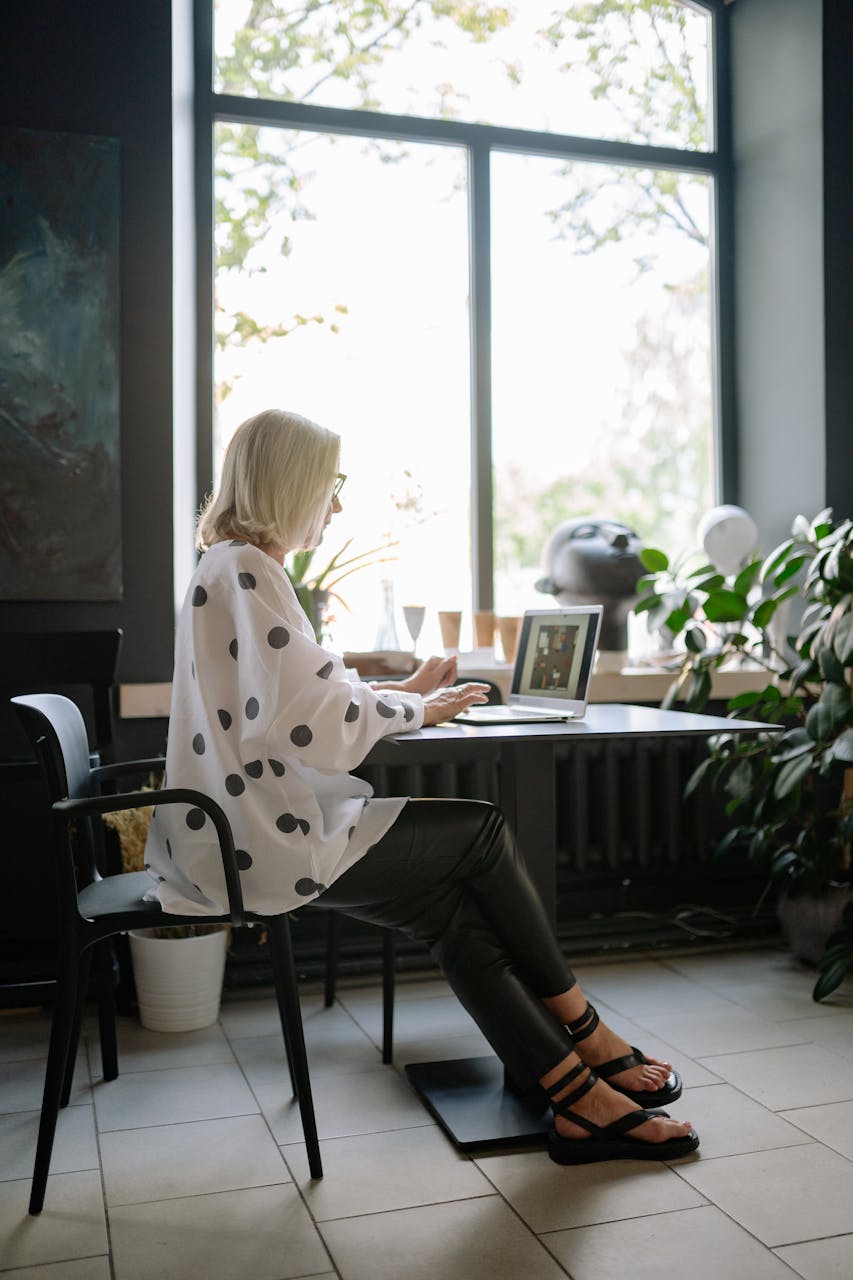 A woman focused on her laptop in a sunlit office with natural decor.