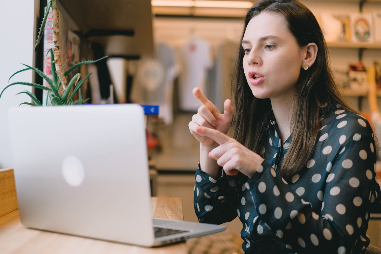 Concentrated young female entrepreneur with long brown hair explaining business strategy while having video conference via laptop during remote work