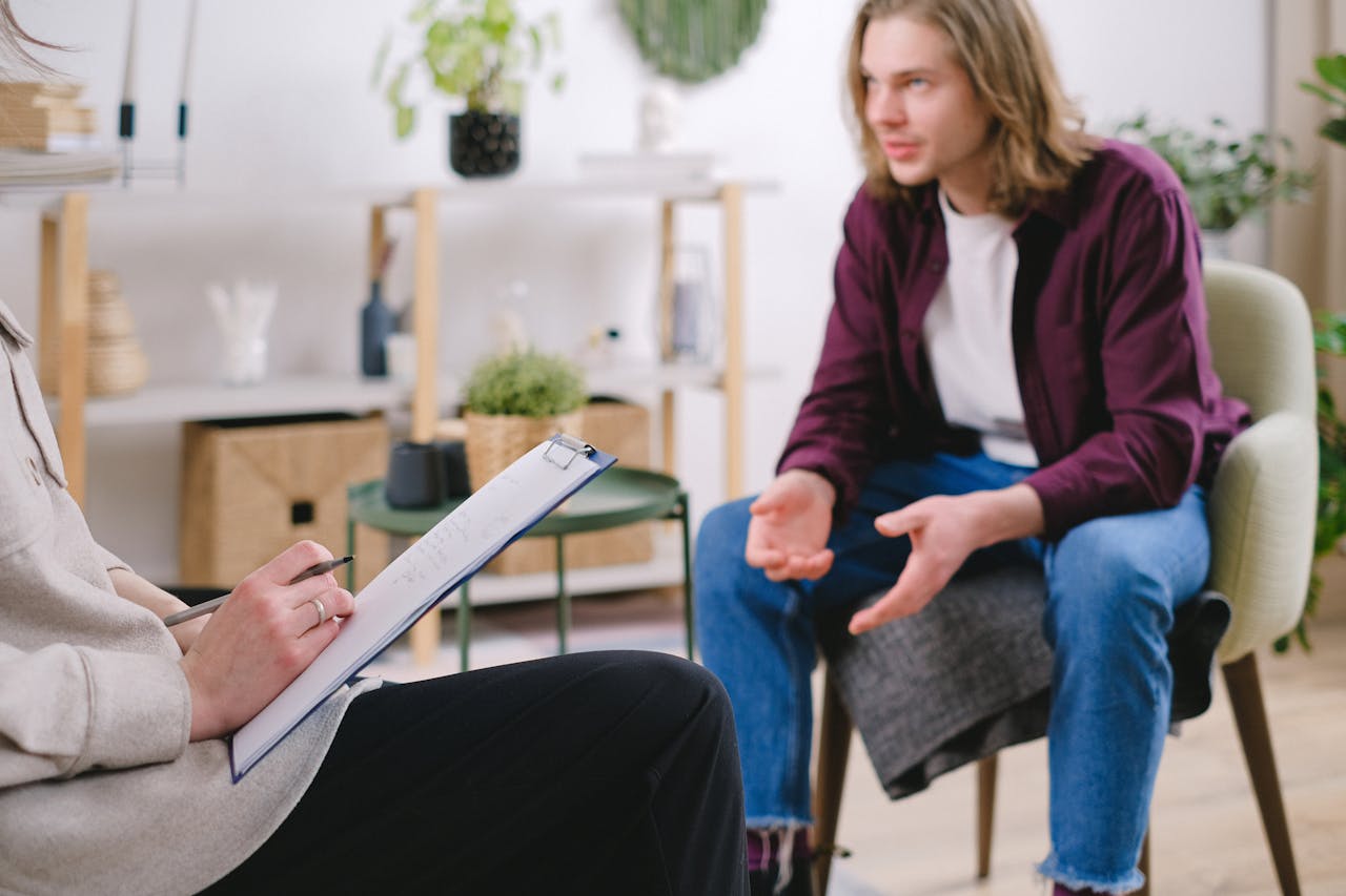 Professional therapy session with a man discussing I-CBT for OCD with a therapist taking notes indoors.