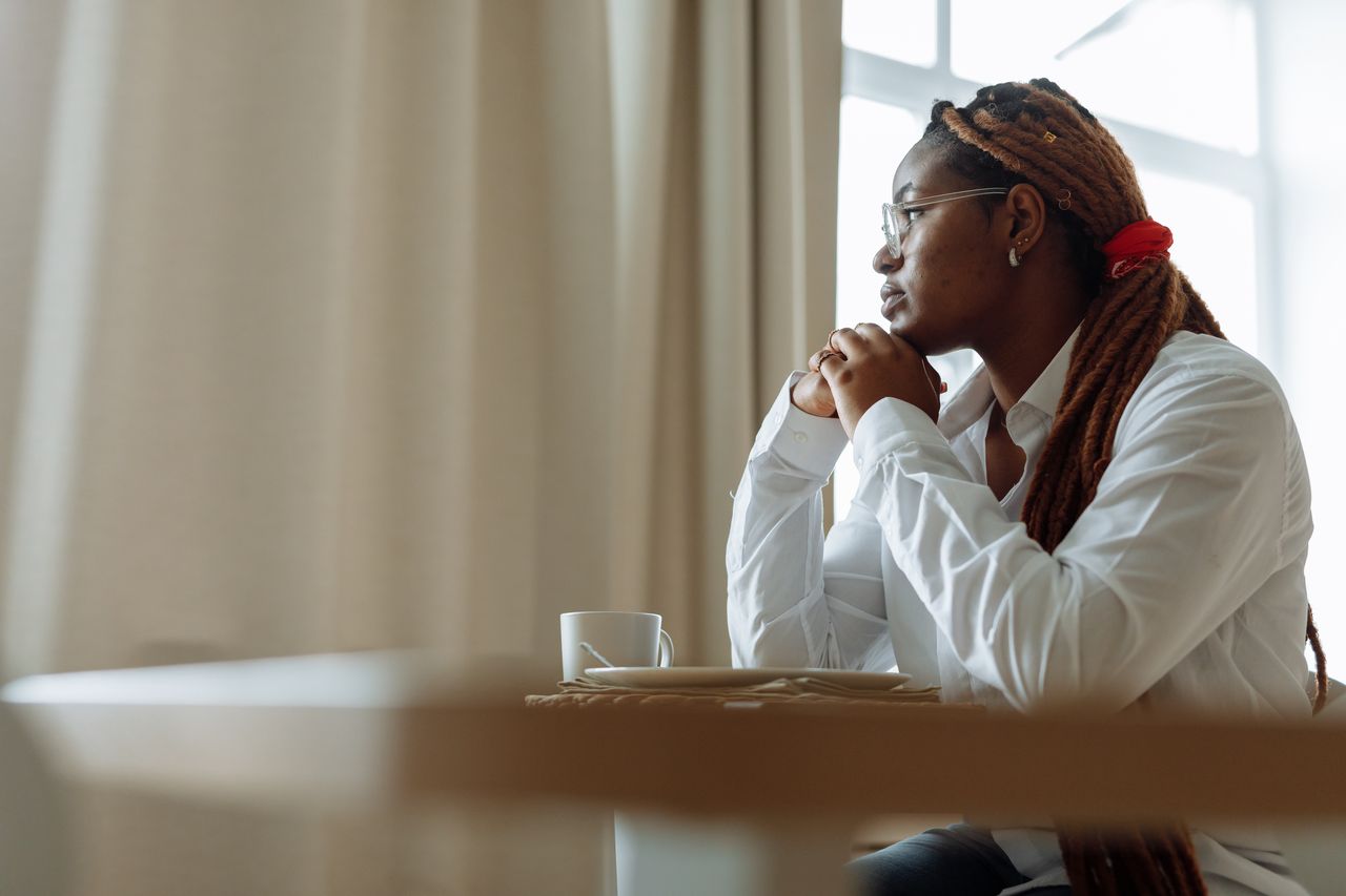 Side view of a pensive person with dreadlocks in a white shirt, enjoying coffee indoors.