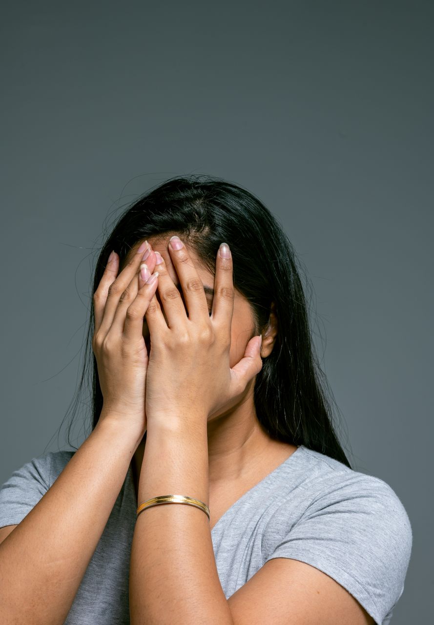 Woman covering face with hands in a studio, expressing sadness and stress.