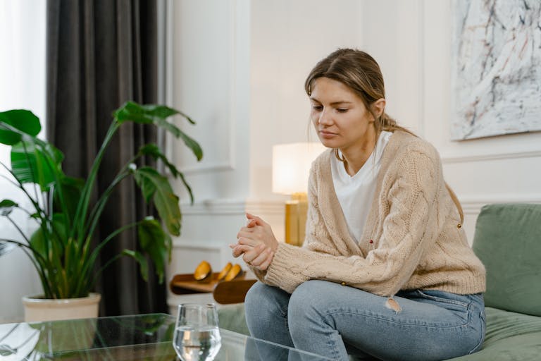Woman sitting on sofa in living room, looking contemplative and relaxed.