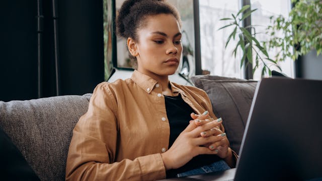 Young woman intently studying on a laptop while seated indoors with natural light.