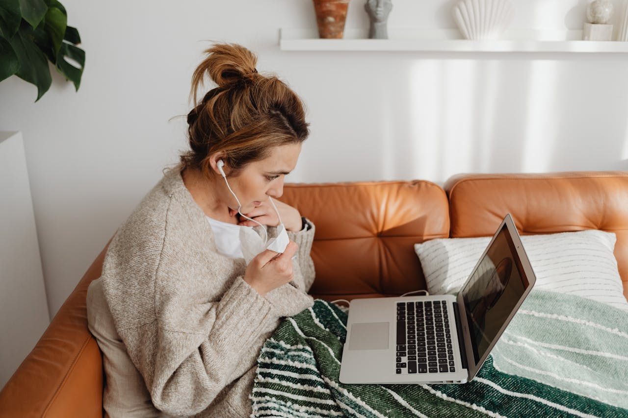 Young woman video chatting on laptop while wrapped in a blanket on a cozy sofa looking for a CBT therapist