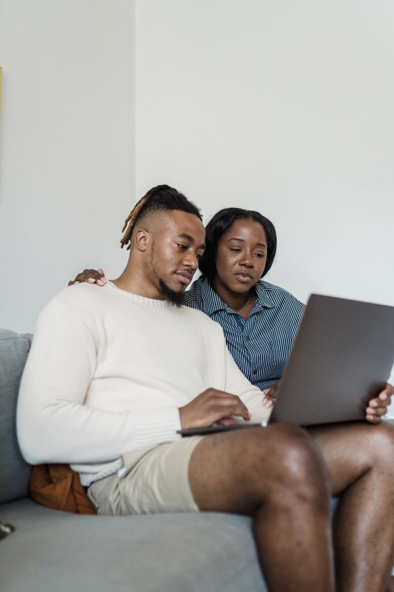 African American couple sitting on a couch using a laptop together, enjoying a cozy moment at home.