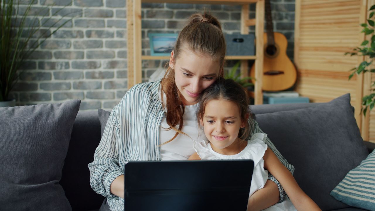 Happy mother and daughter bonding while using a laptop in a cozy living room setting.