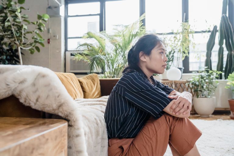 Asian woman sitting thoughtfully indoors with lush plants and natural light.