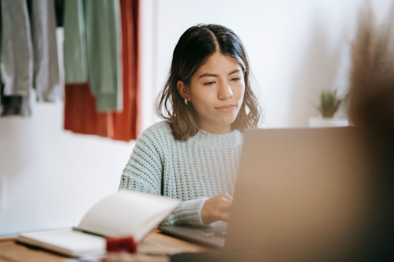 Content young focused ethnic female browsing netbook at table with notebook in soft focus