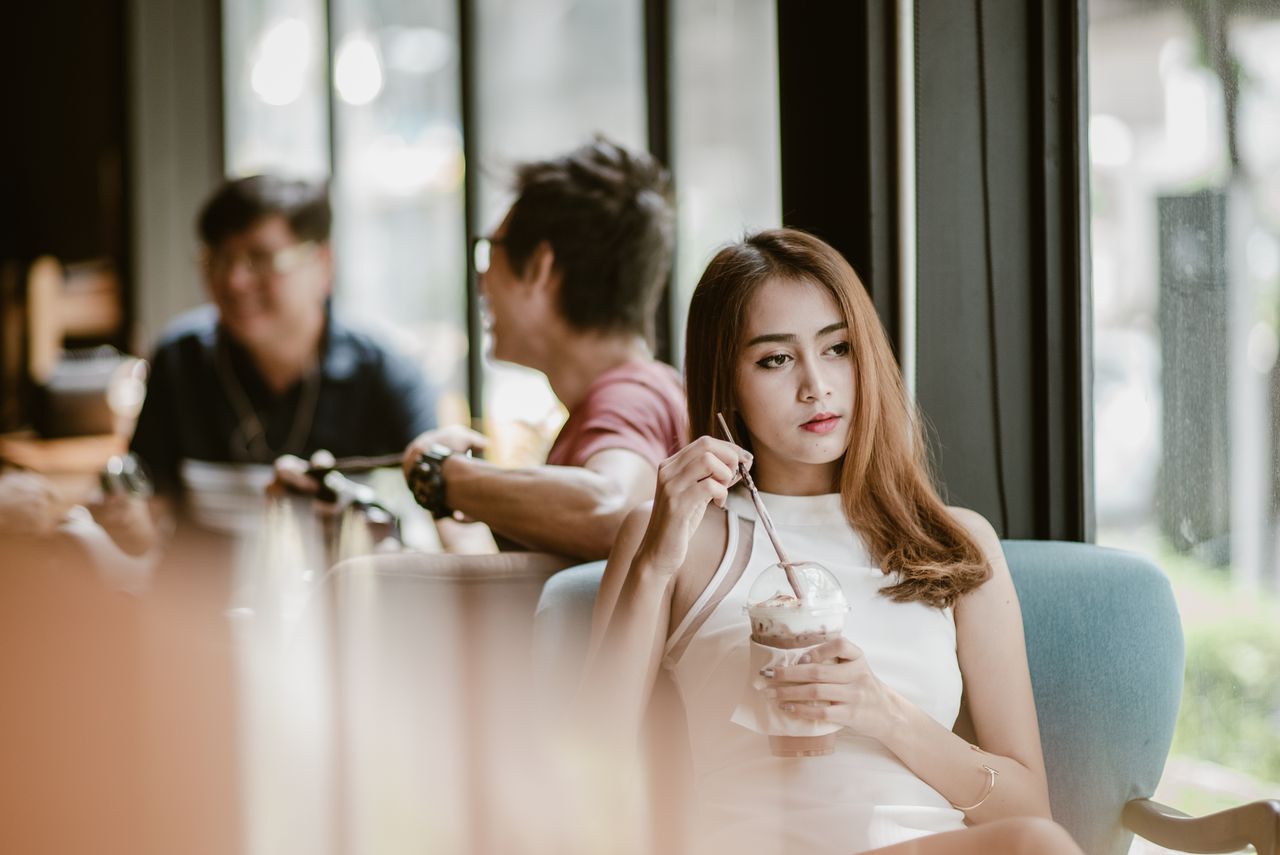 Young woman in a white dress enjoying a beverage in a modern cafe.