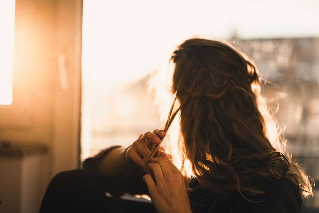 A woman sitting indoors, backlit by sunlight, playing with her messy hair.