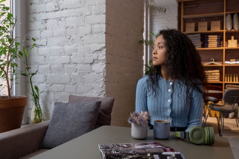 Young woman in a blue sweater enjoying a peaceful moment in a cozy cafe setting with a drink.