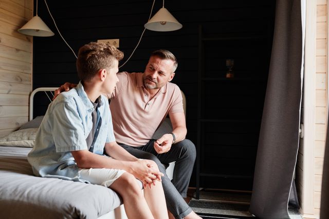 A father bonding with his teenage son in a cozy bedroom, sharing advice and conversation.