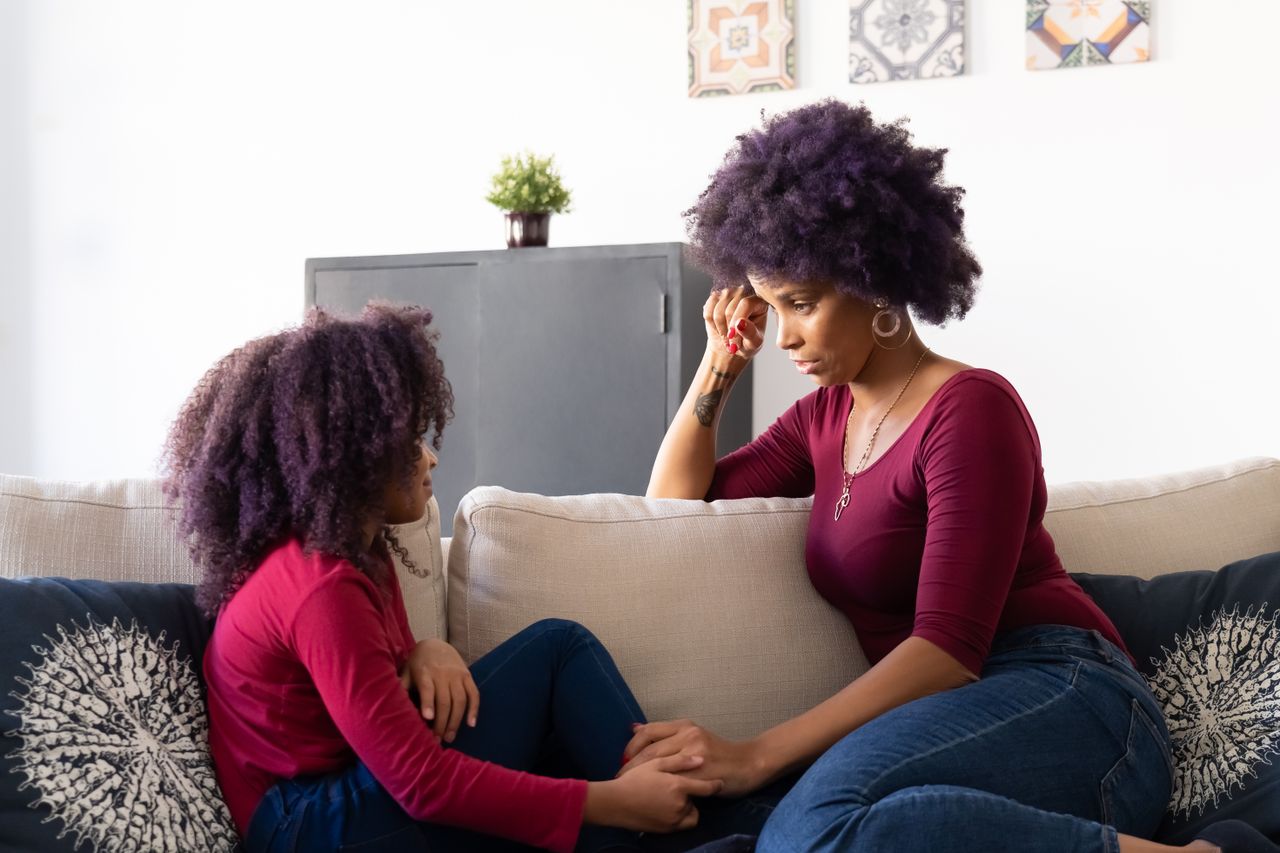 A mother and daughter sitting on a sofa, sharing an affectionate moment indoors.