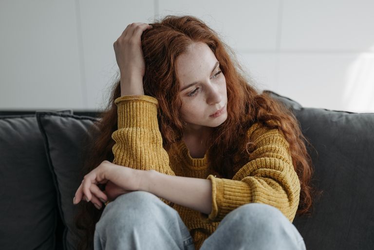 A young woman with red hair sits thoughtfully on a couch, expressing introspection indoors.