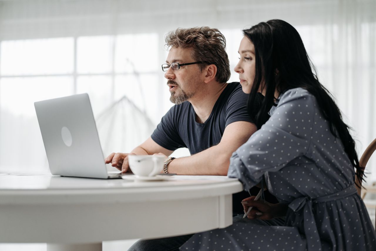 A couple uses a laptop at home in a bright and cozy setting, collaborating closely.