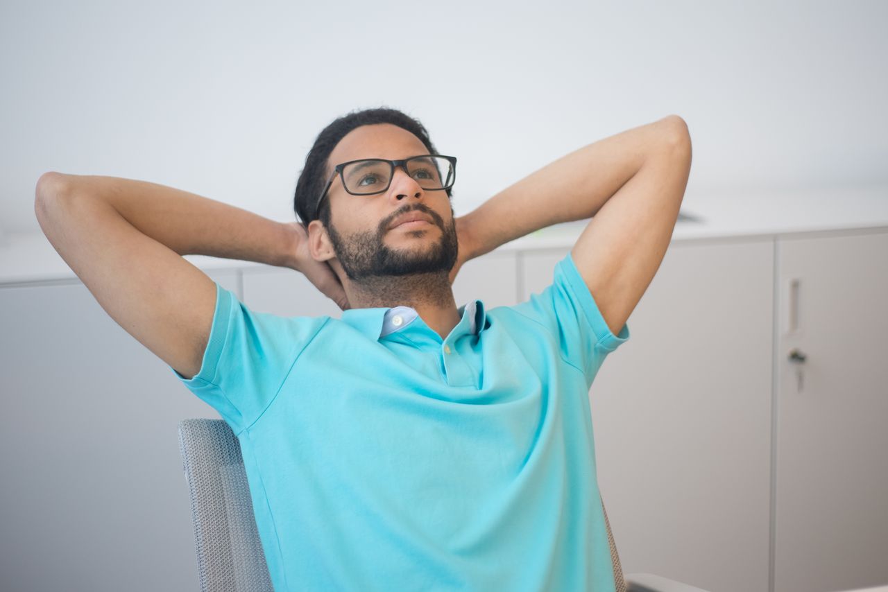 A thoughtful man in a blue polo shirt relaxing indoors, wearing eyeglasses.