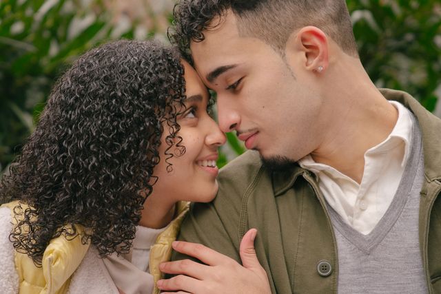 Happy ethnic crop couple hugging and looking to each other while spending time together in park and smiling at daytime