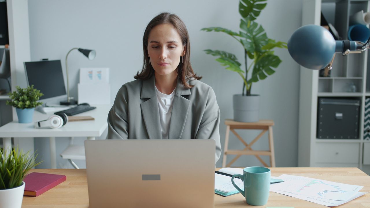 Woman working at a desk in a modern office environment, focused on her laptop.