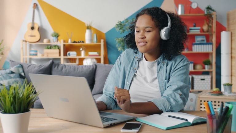 Young woman working remotely on laptop in colorful home office setting.